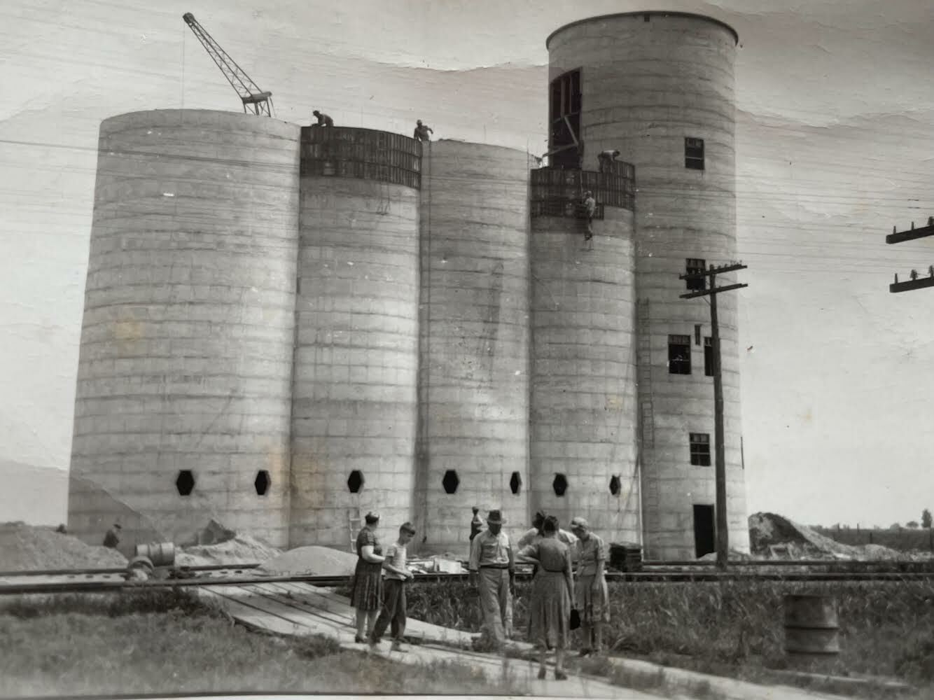 Historic black and white photo of the rice dryer under construction, with workers in front of the silos