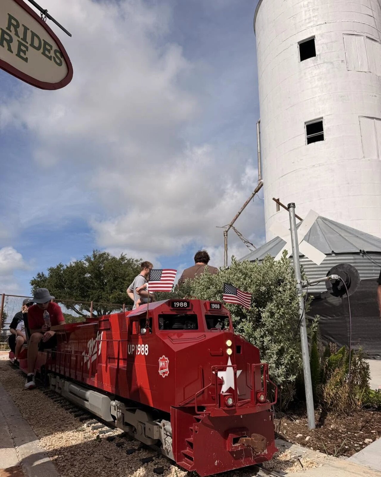 The red "The Katy" engine with flags and riders in front of the silo